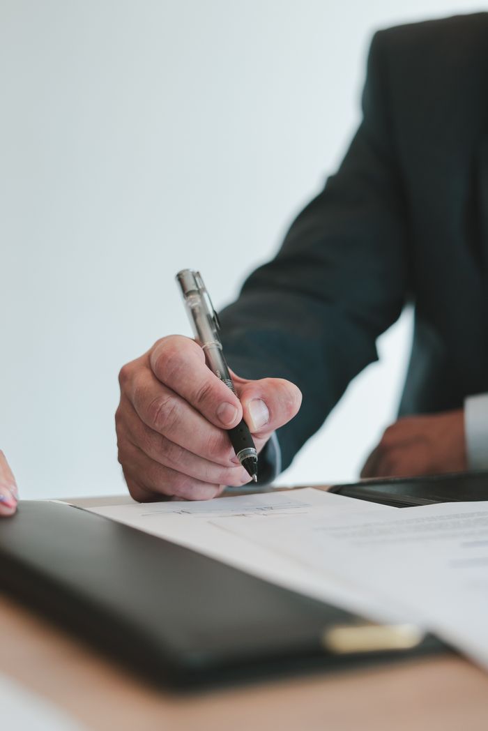 Offerings A businessman in a suit signing a contract in an office setting, emphasizing professional context.